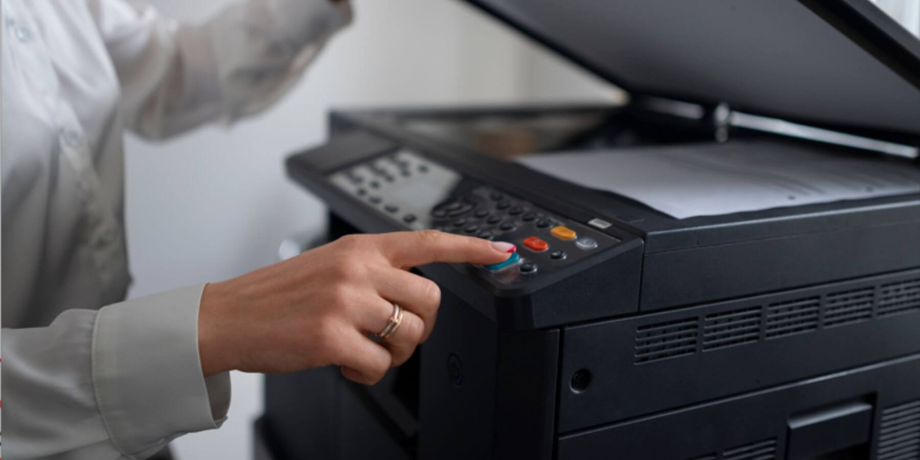 A woman's hand pressing the start button on a scanner machine, initiating the scanning process.