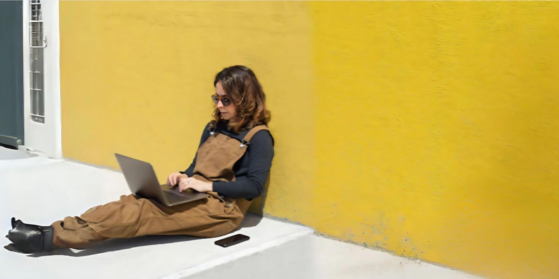 A woman seated on the floor, engaged in work on her laptop.